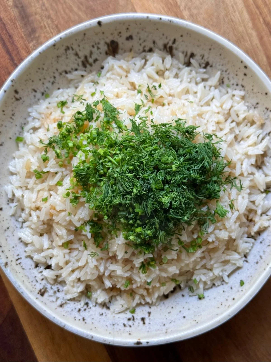 A bowl of herby brothy rice topped with chopped dill and chives