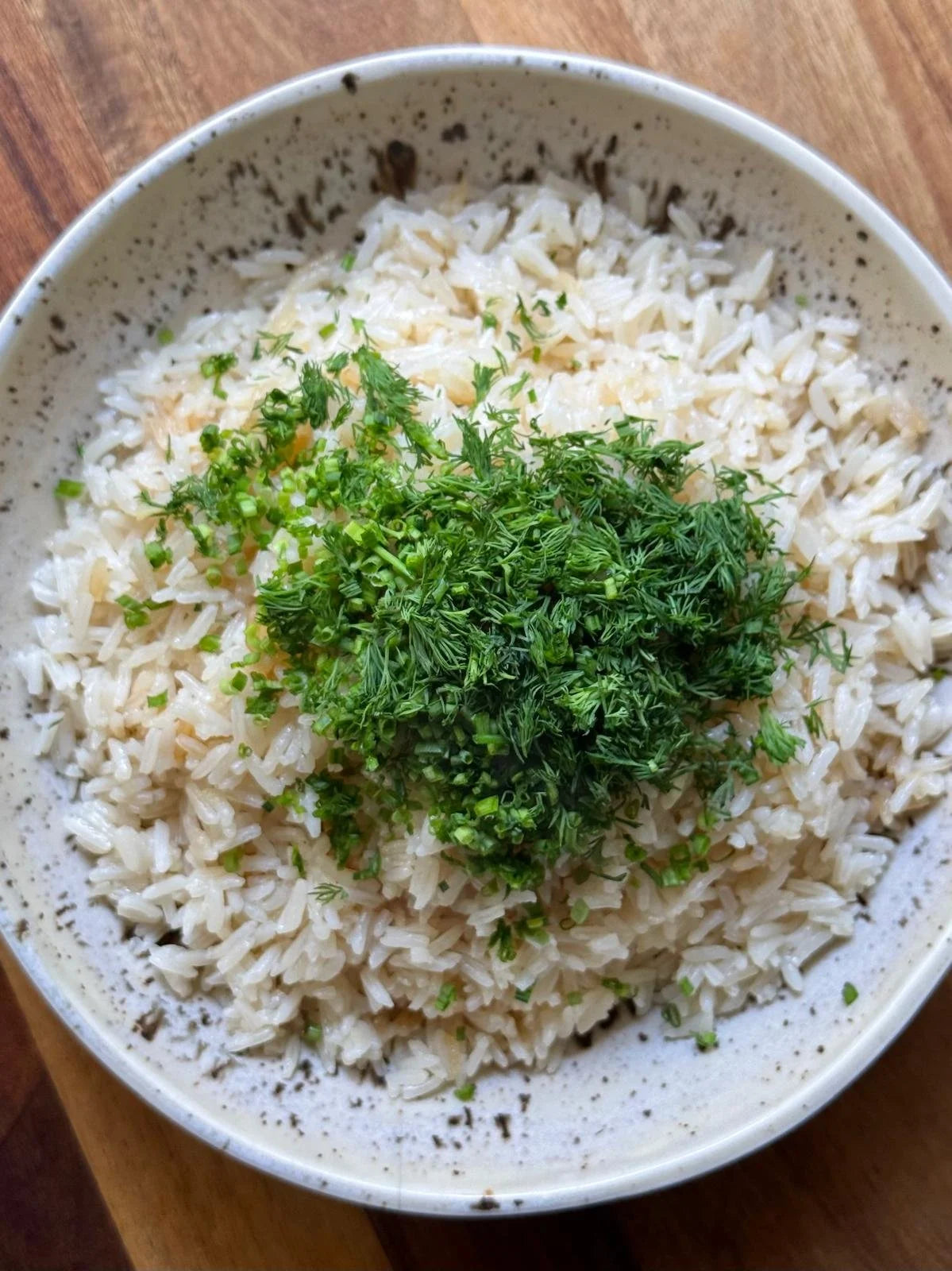 A bowl of herby brothy rice topped with chopped dill and chives